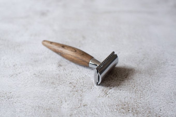 A safety razor with a wooden handle resting on a concrete surface