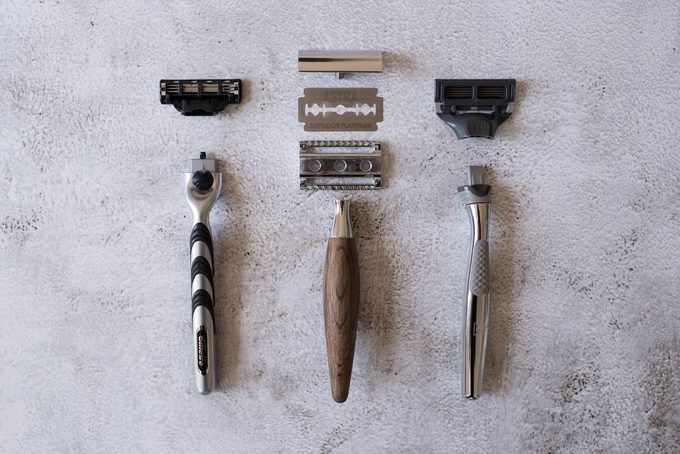 Flat lay comparing a disassembled safety razor with wooden handle and Astra blade (centre) against cartridge razors (left and right)